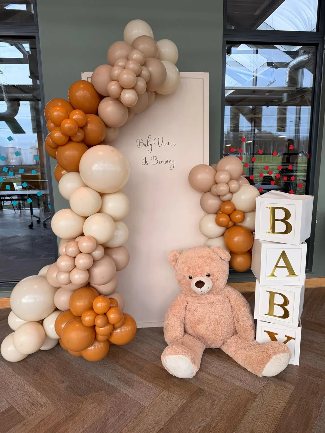 A baby shower with a tan and cream balloon garland, a teddy bear and baby letter blocks