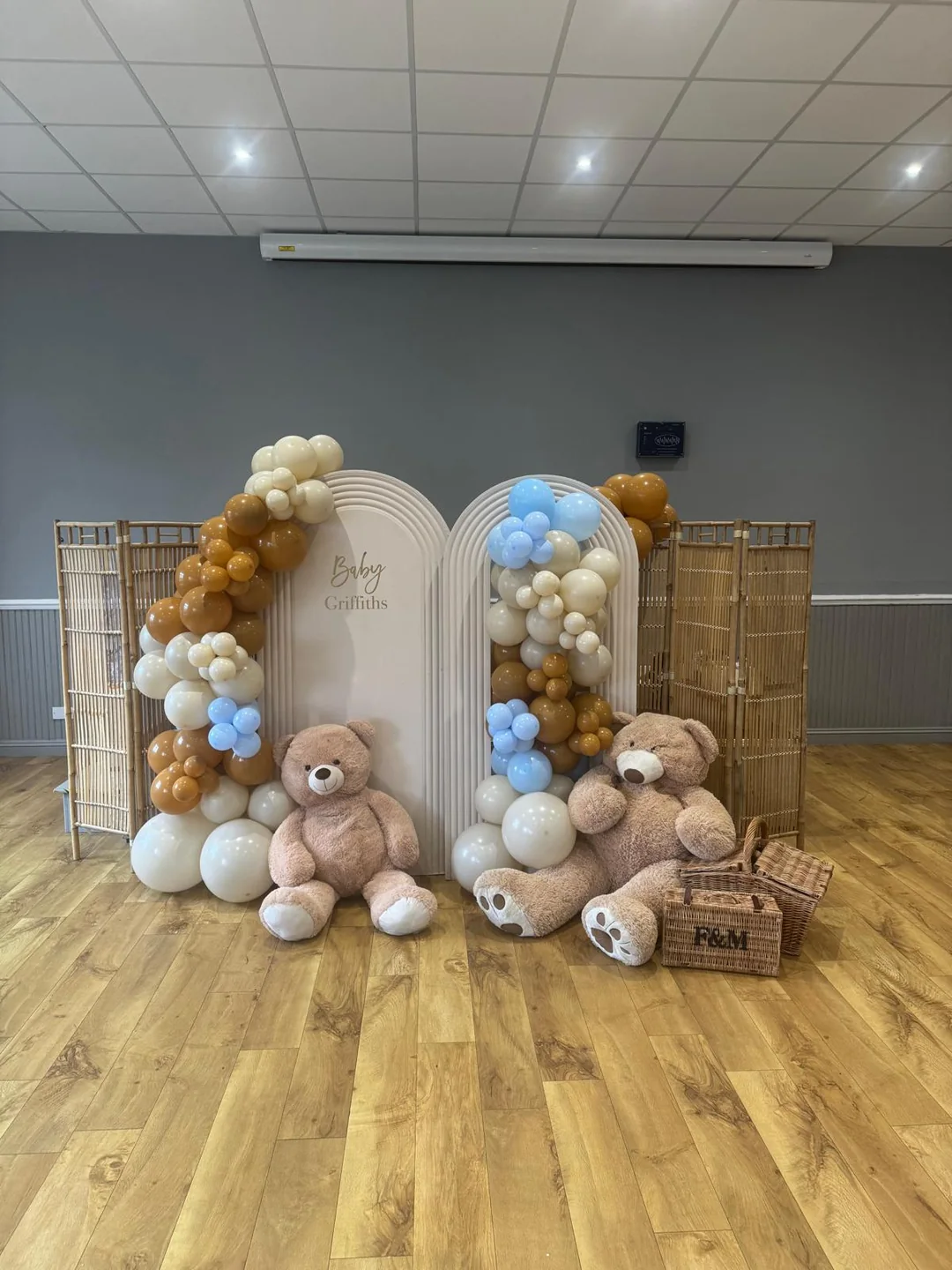 A baby shower with arched backdrops, a tan and blue balloon garland and teddy bears