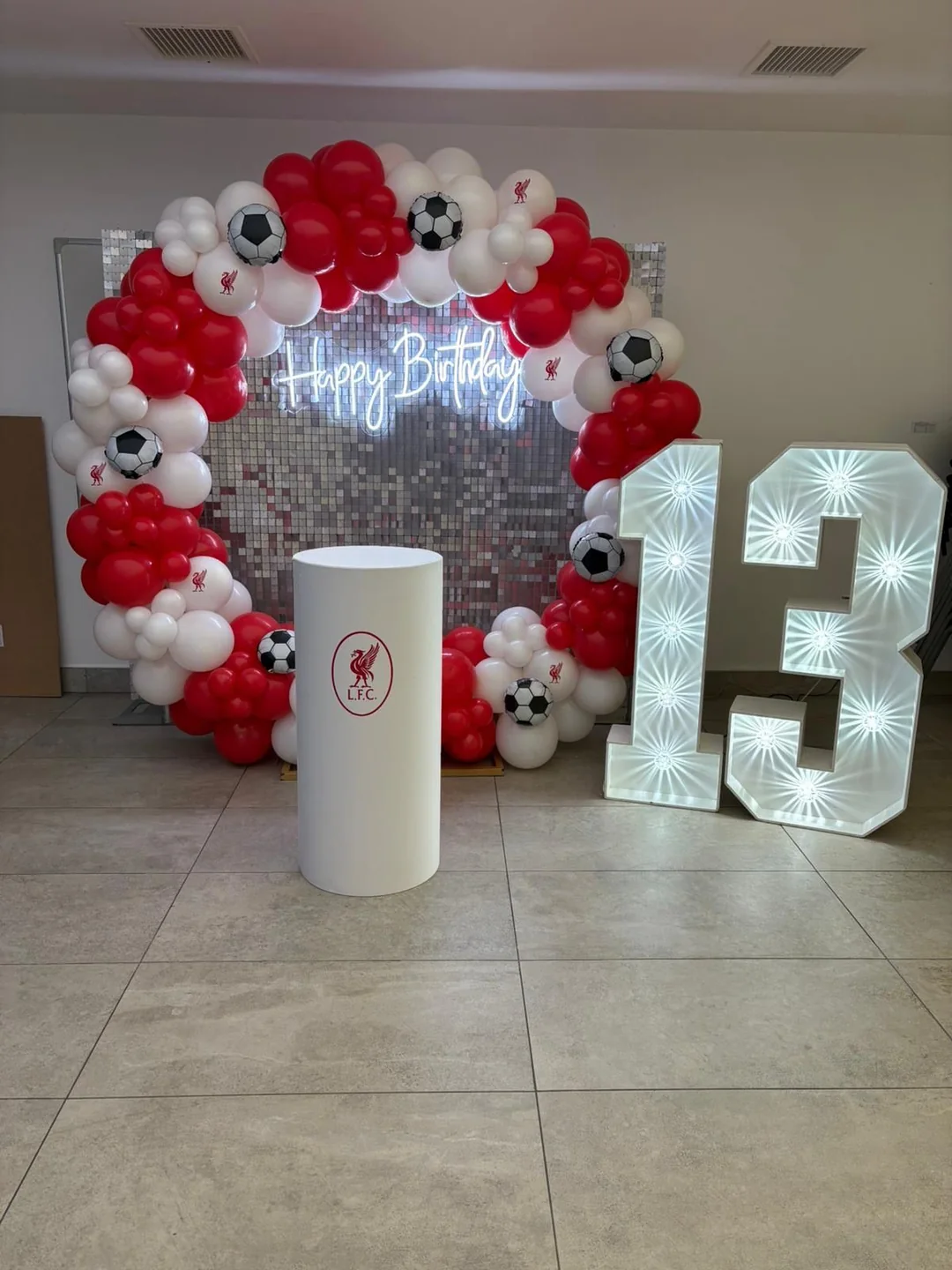 A football themed thirteenth birthday with a silver sequin wall, a red and white garland and a light up 13