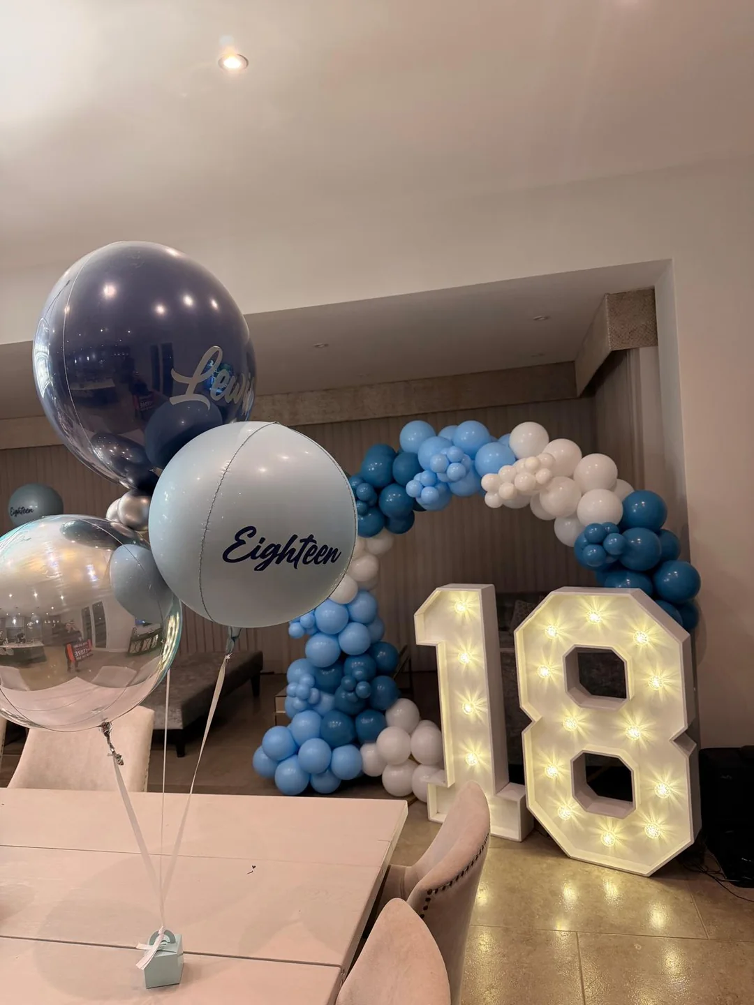 A light up 18 with a blue and silver balloon garland and a personalised bubble balloon