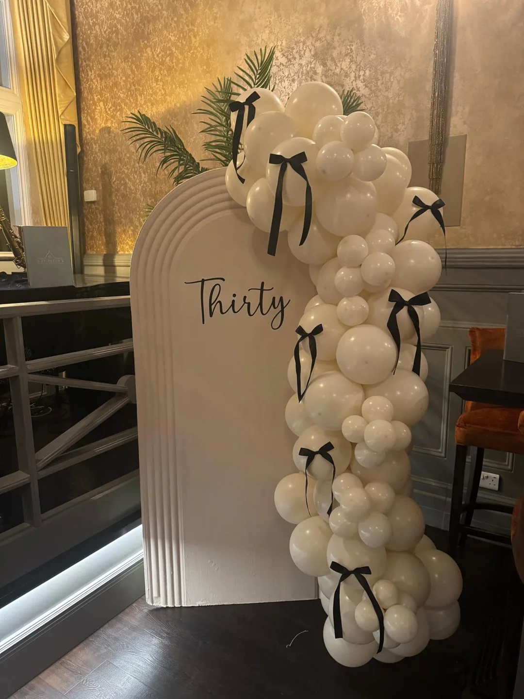 A cream balloon garland tied with black bows around an arched backdrop reading Thirty