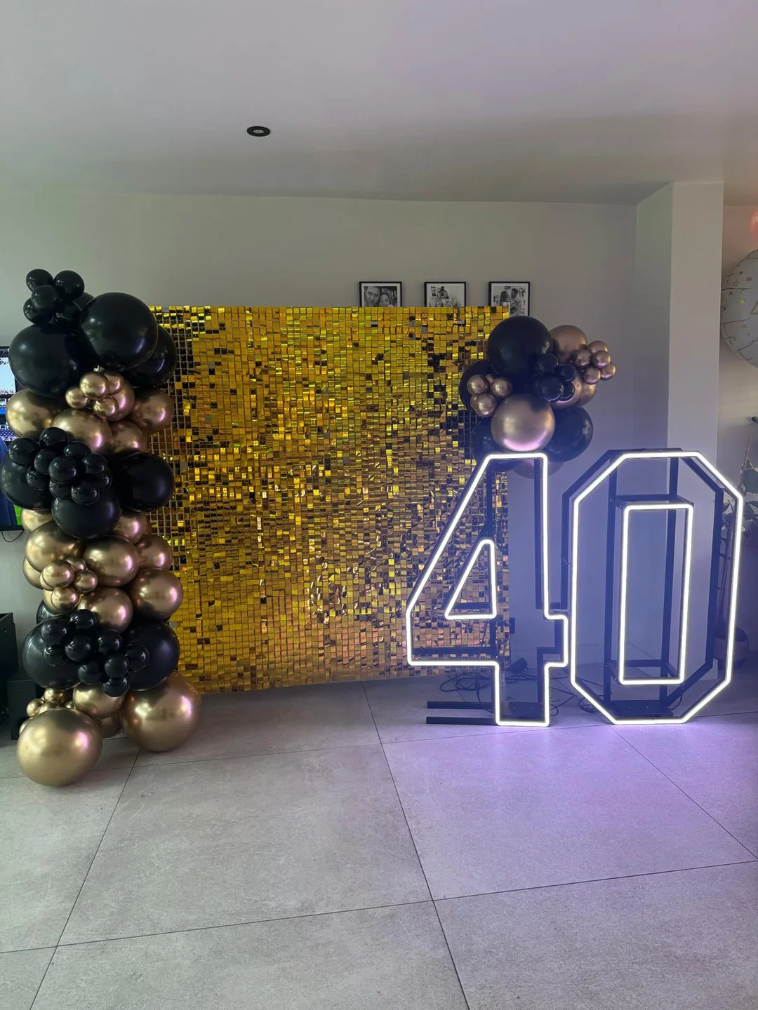 A gold sequin wall with a black, gold and rose balloon garland and a light up 40