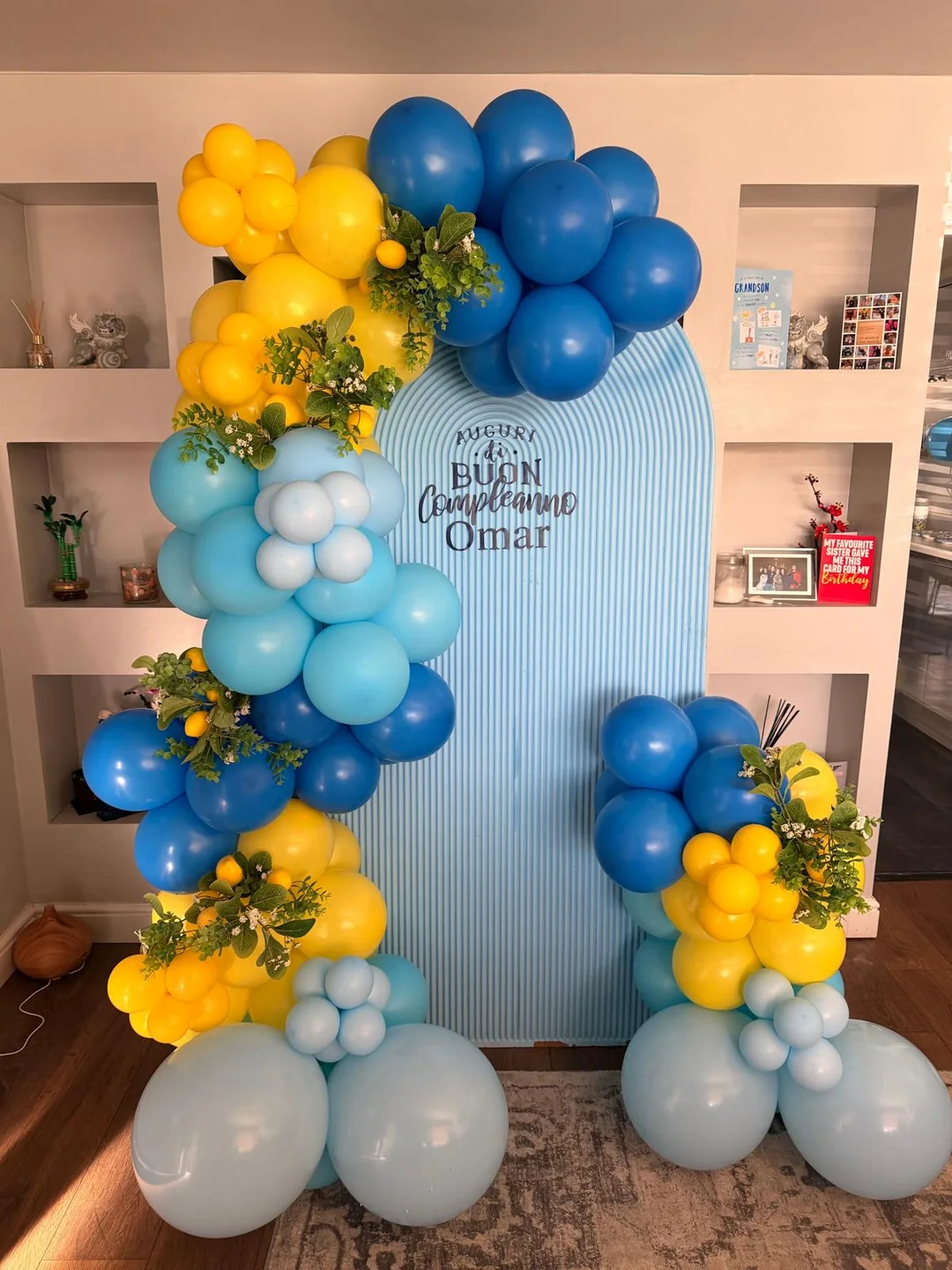A blue and yellow balloon garland with greenery around a fluted backdrop
