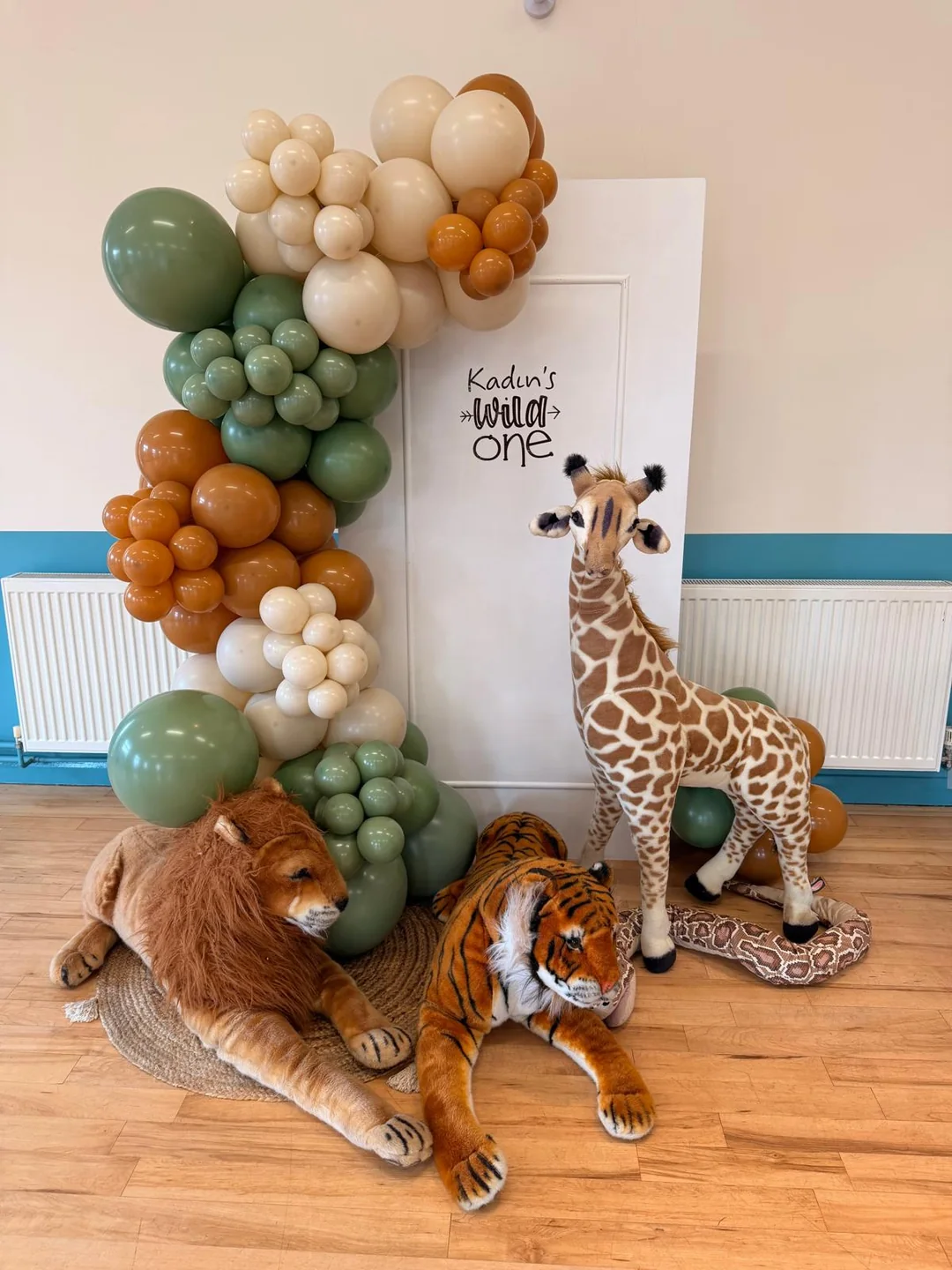 A safari first birthday with a sage and brown garland and giraffe, lion and tiger props