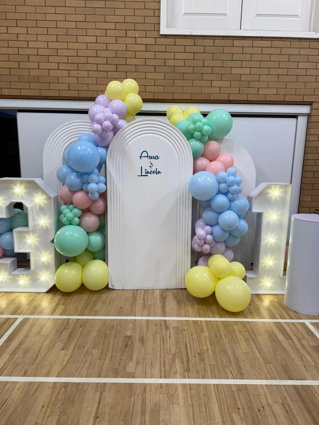 Two light up number ones with a pastel balloon garland across a pair of arched backdrops