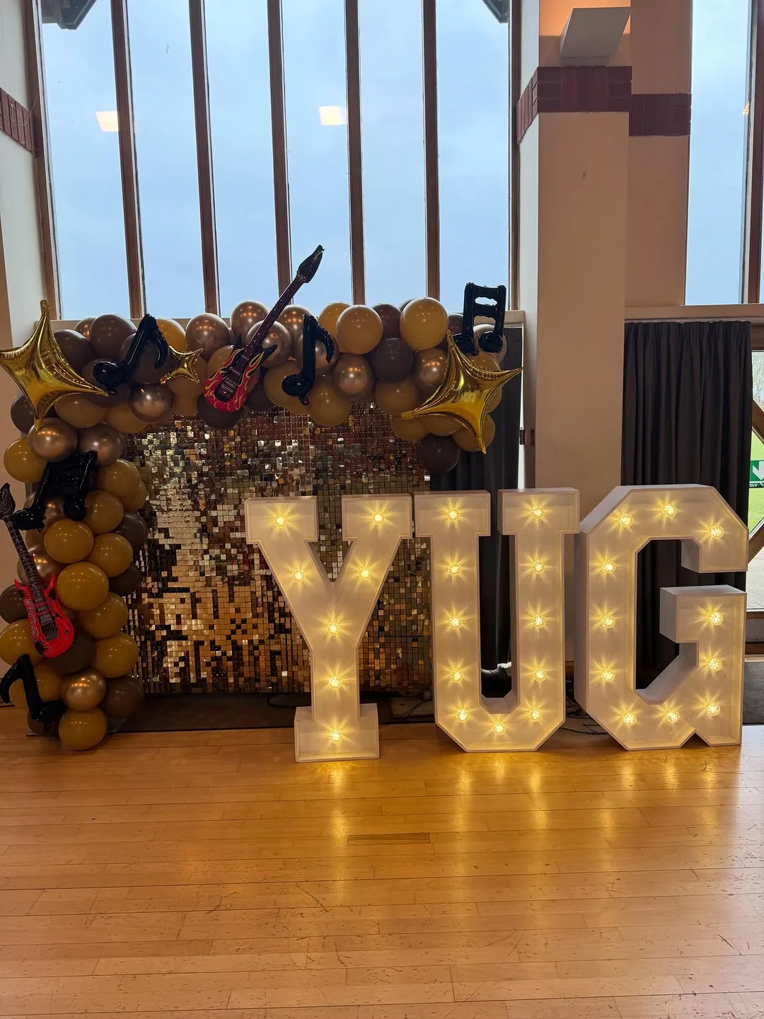 Light up letters spelling YUG against a gold sequin wall