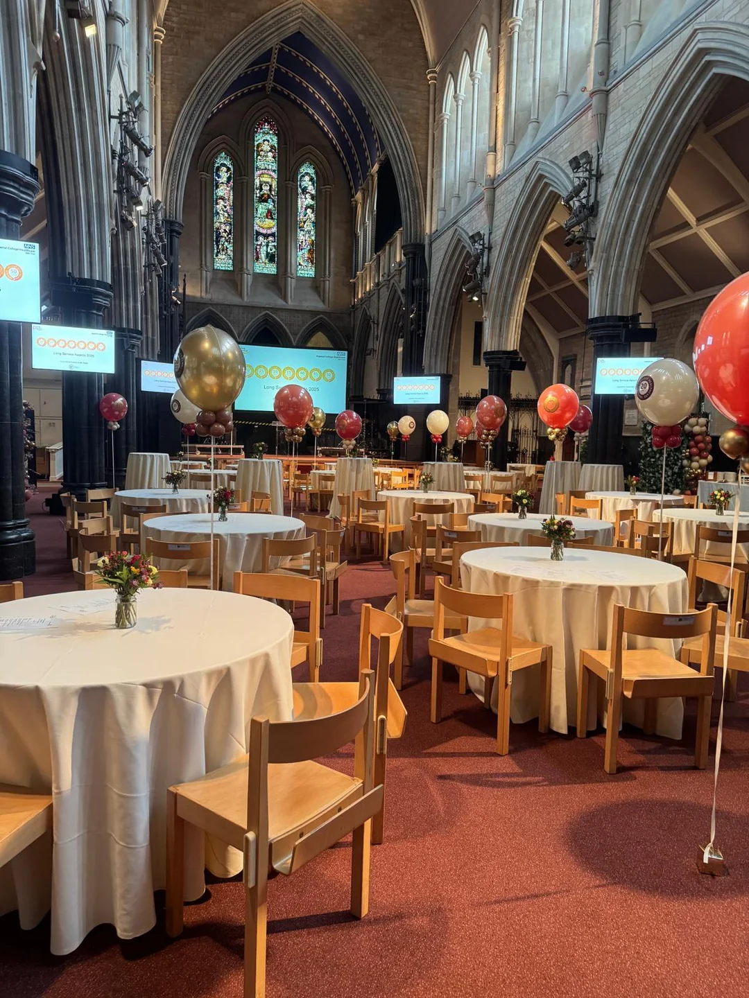A church laid with round tables, cloths and balloon bouquets for a family service
