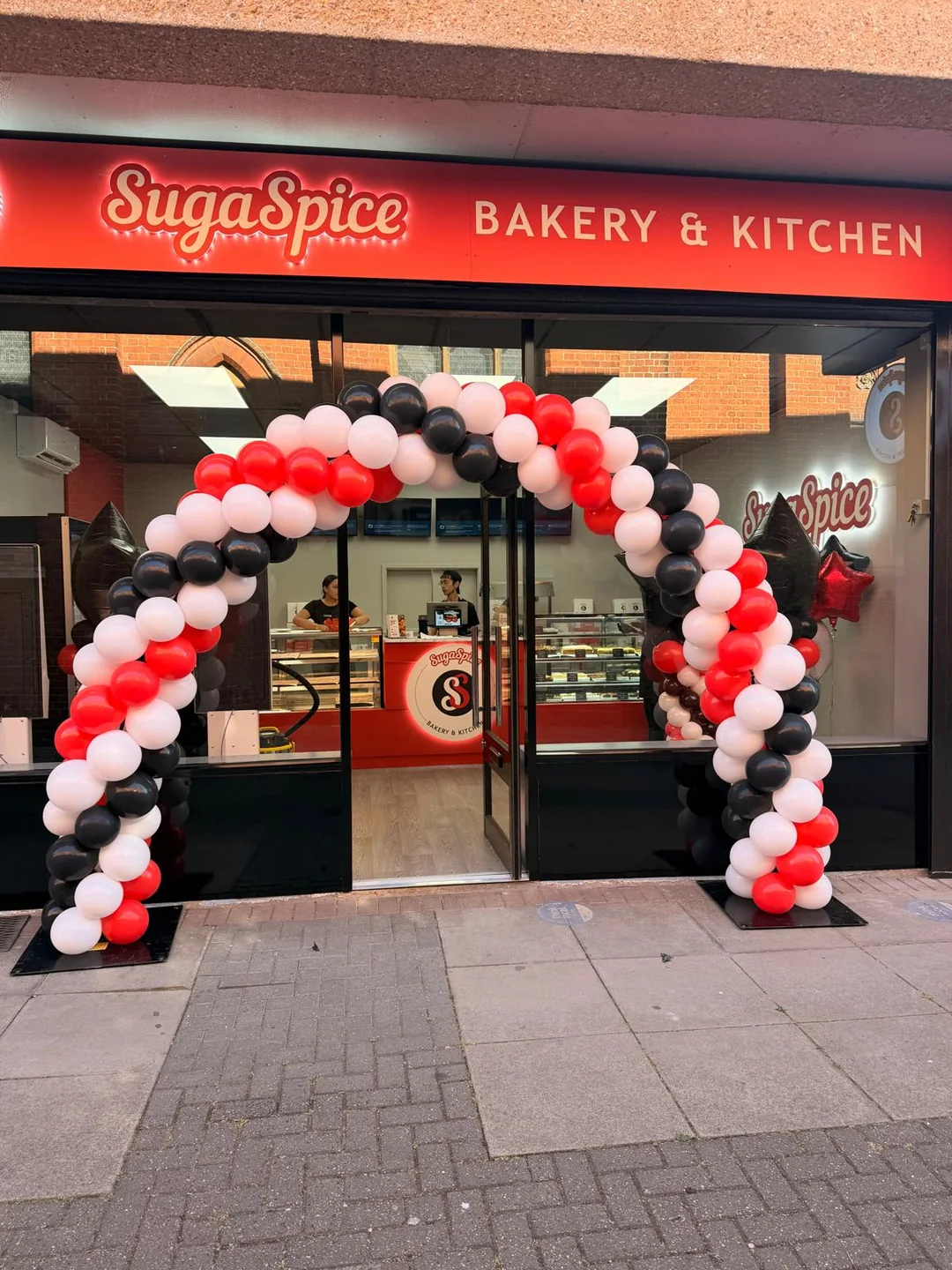 A red, white and black balloon arch over the front of a bakery for its opening