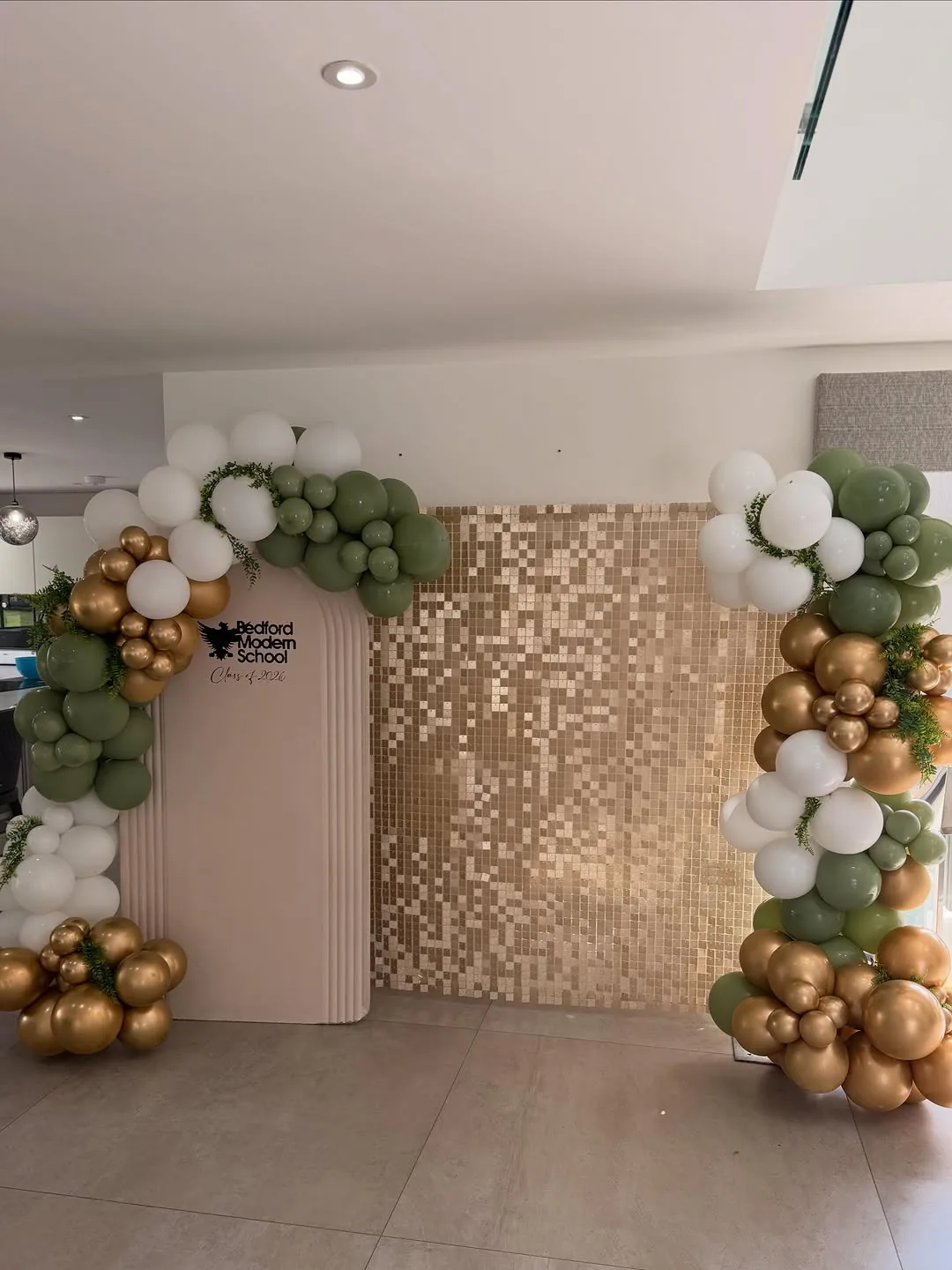 A gold and sage garland framing a sequin wall at a school event