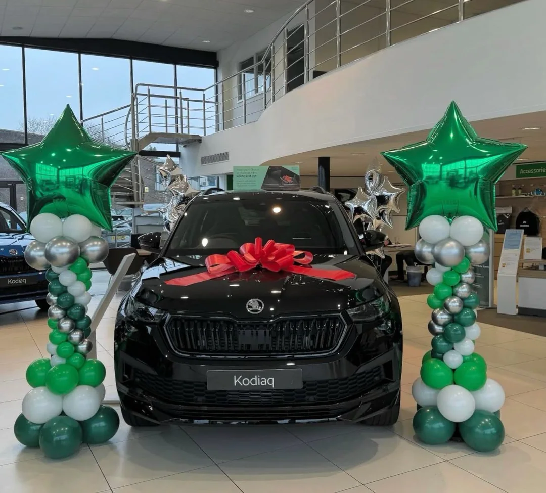A new car in a showroom dressed with a red bow and green and white balloon columns