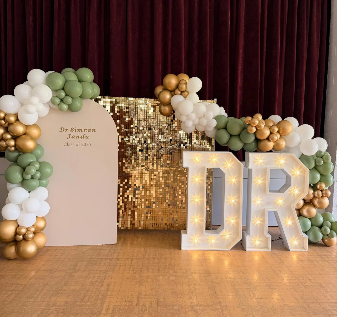 A graduation display with a gold sequin wall, a sage and gold garland and light up letters
