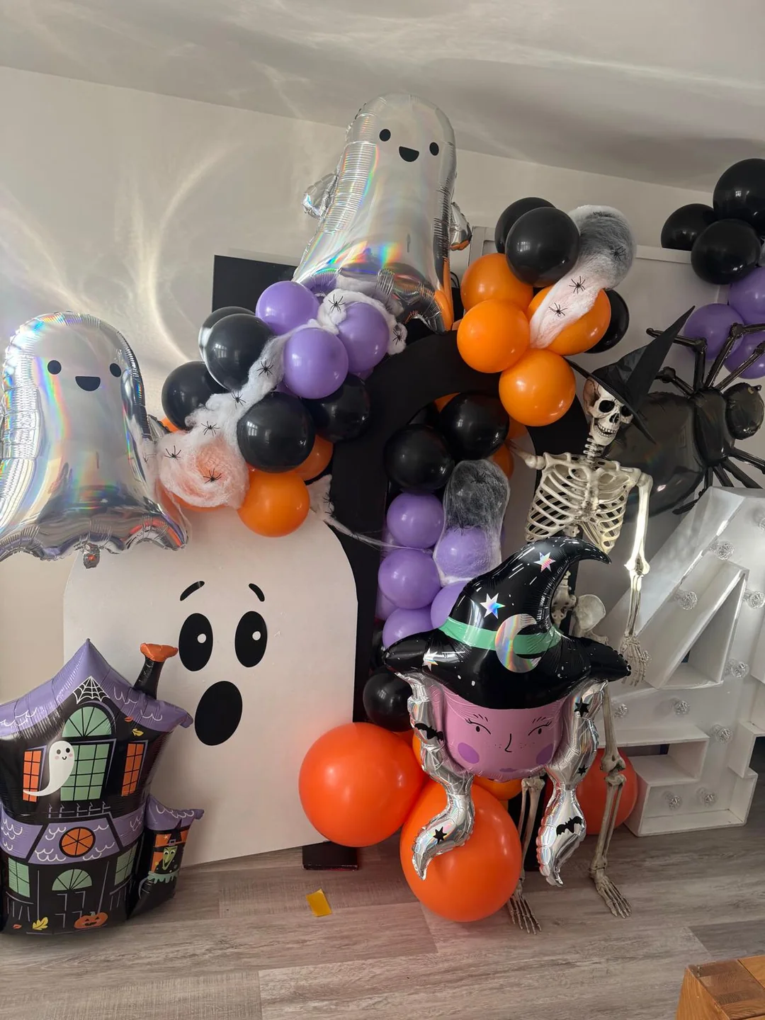A Halloween display with ghost foil balloons, a skeleton and an orange, black and purple garland