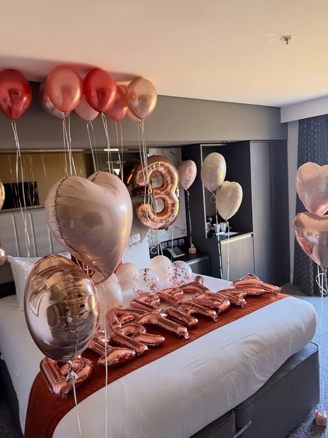A rose gold birthday balloon display arranged across a bedroom