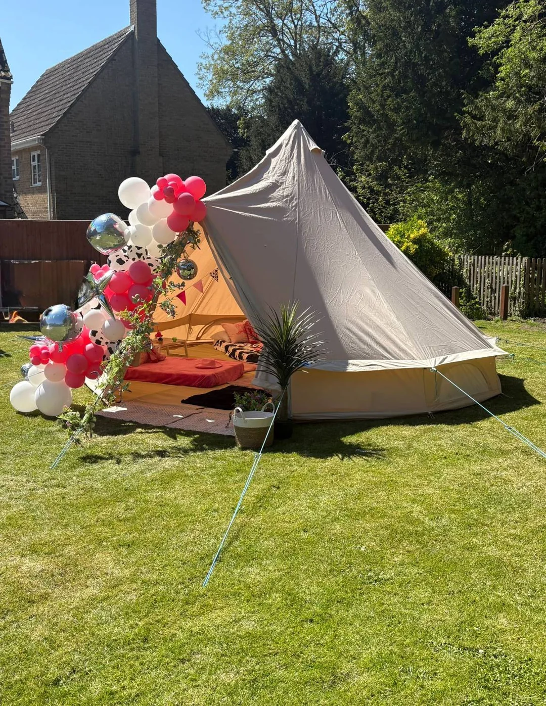 A bell tent pitched on a lawn with a pink, white and cow print balloon garland and disco balls over the entrance