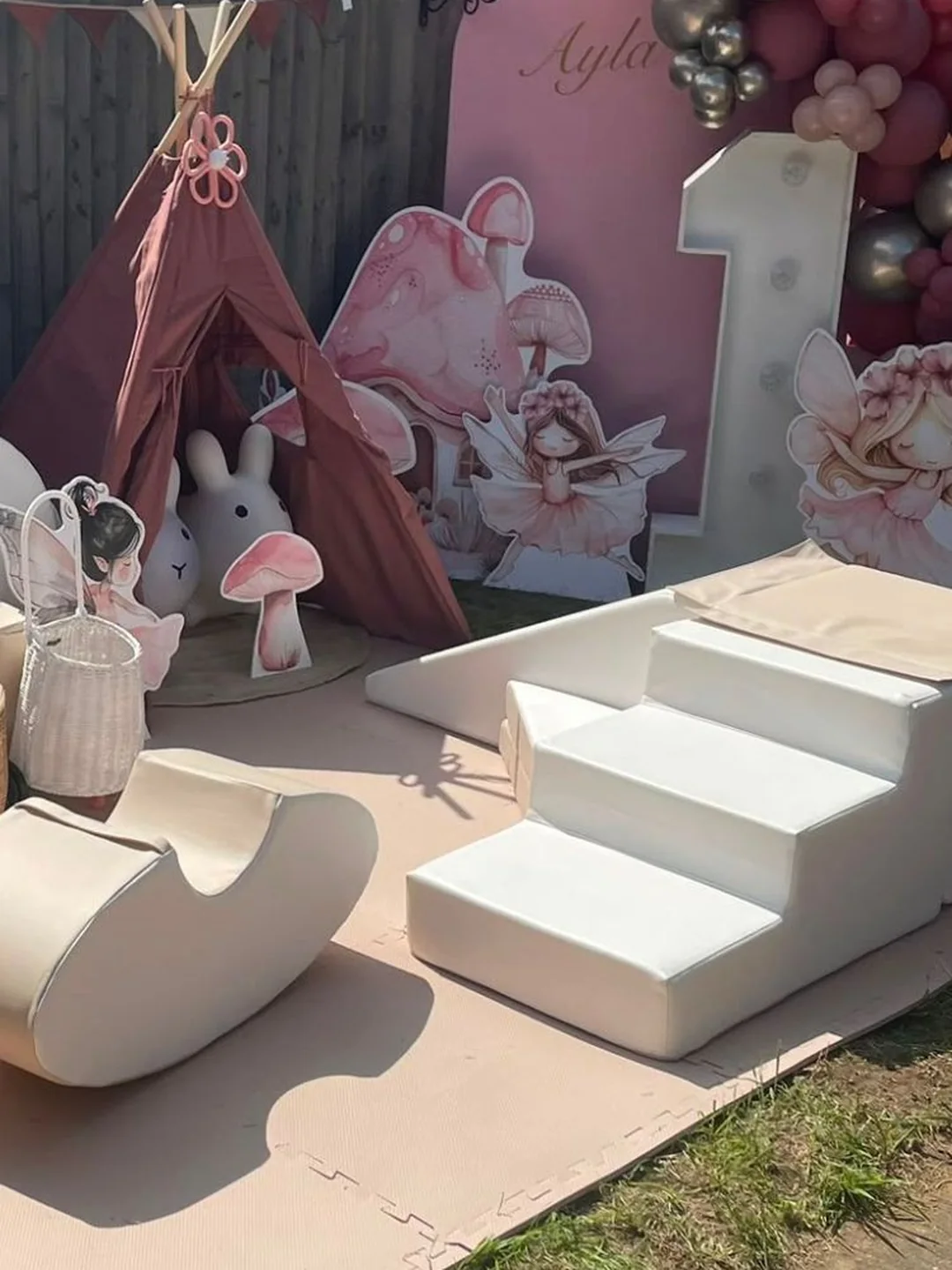 A dusty pink teepee and a fairy backdrop with a light up number one behind cream soft play