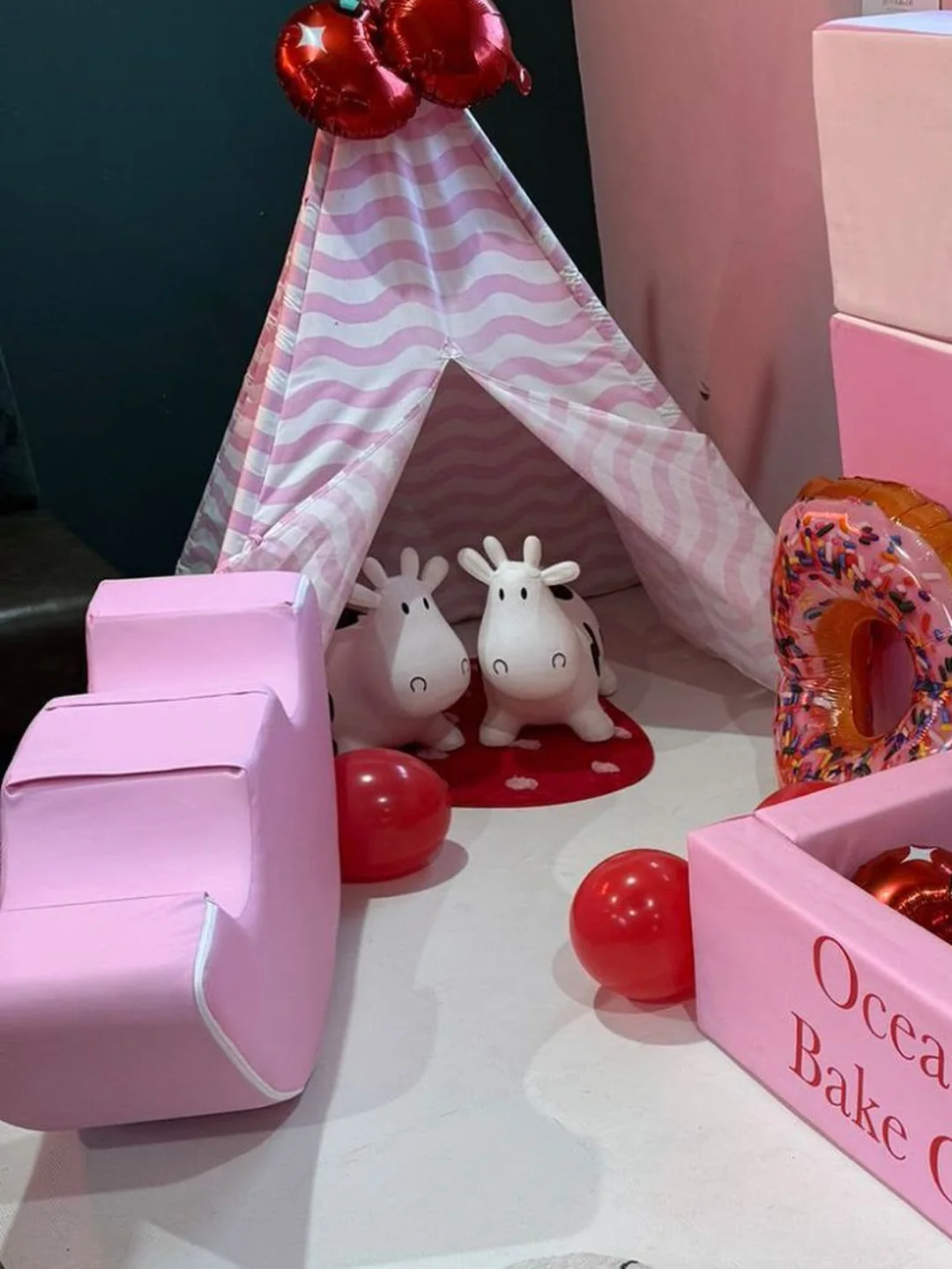 A pink striped teepee, cow ride on toys and pink soft play steps beside a ball pit