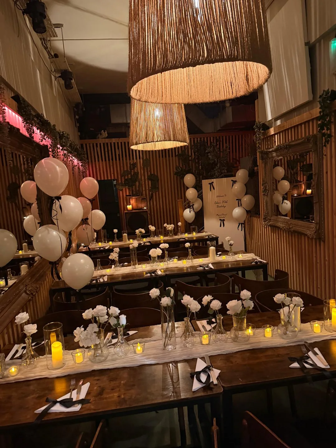 A long restaurant table dressed with white floral stems and candles under pendant lights